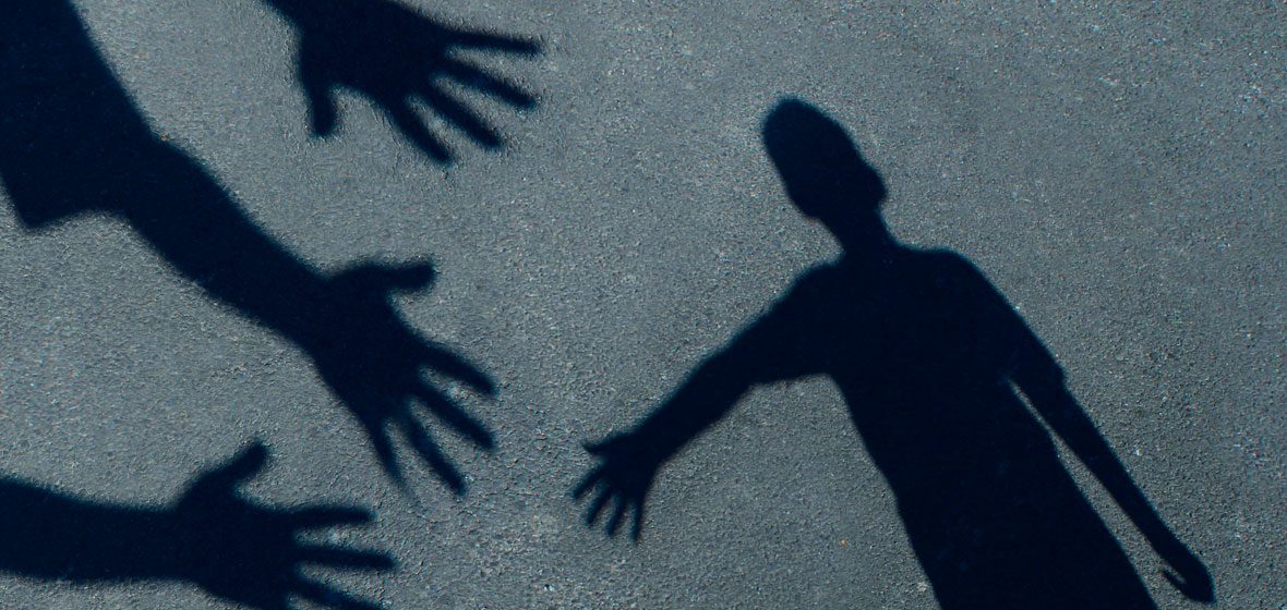 child's shadow on the ground reaching towards several outstretched hands