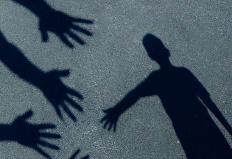child's shadow on the ground reaching towards several outstretched hands