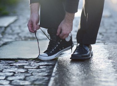 Man tying running shoe on right foot while wearing business shoe on left foot