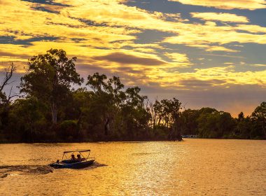 Bush surrounding a lake at sunset. A small boat sails across the lake.