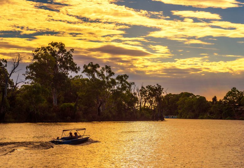 Bush surrounding a lake at sunset. A small boat sails across the lake.