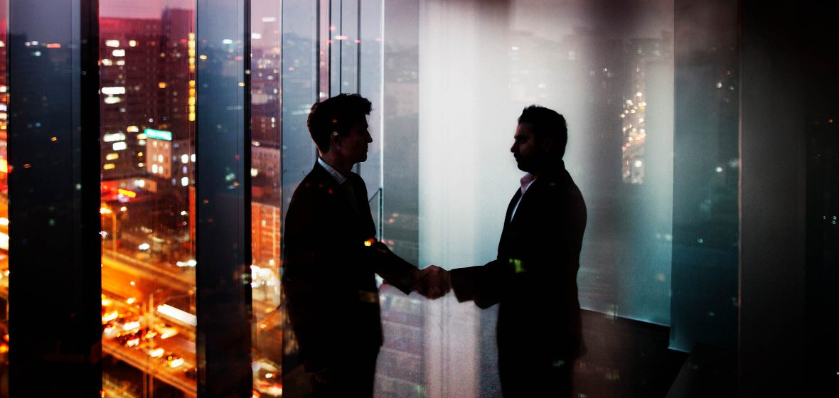 Two men shake hands in a darkened office