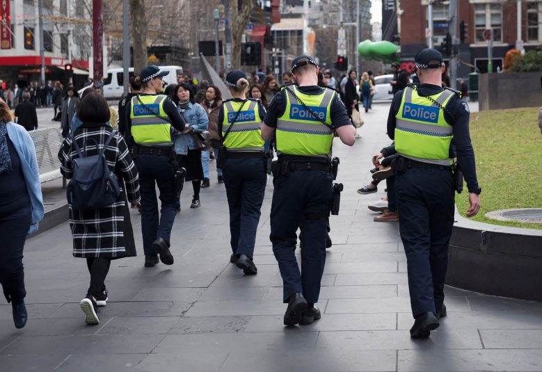 Four police walking down a street among pedestrians