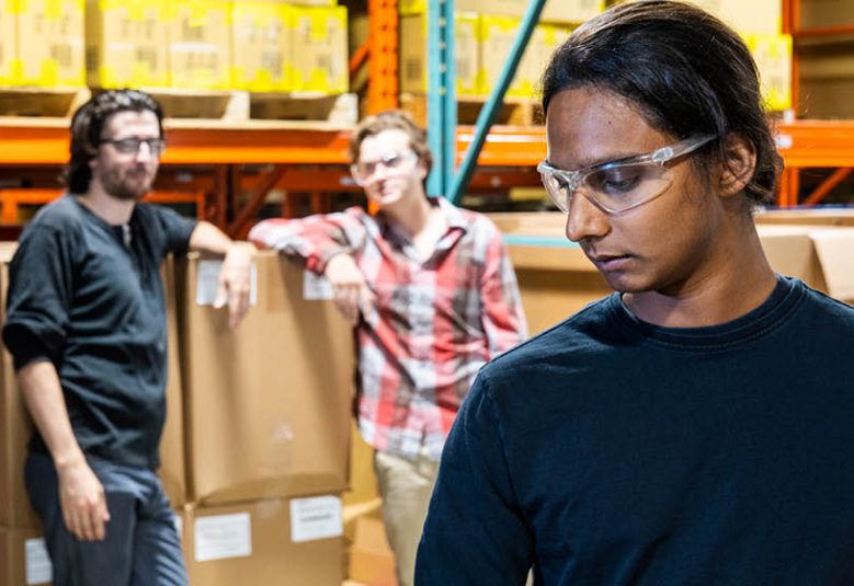 Two male workers look at one female worker in a warehouse setting