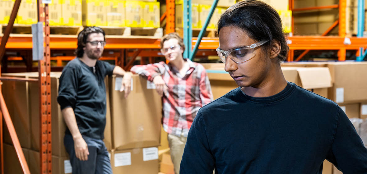 Two male workers look at one female worker in a warehouse setting