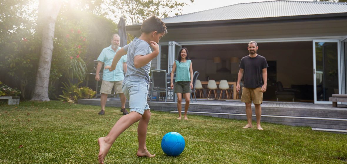 Child playing soccer with family in backyard of house