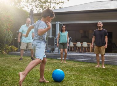 Child playing soccer with family in backyard of house