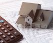 Scale model of a house sits on top of a a checklist on a desk, next to a pencil and a calculator.