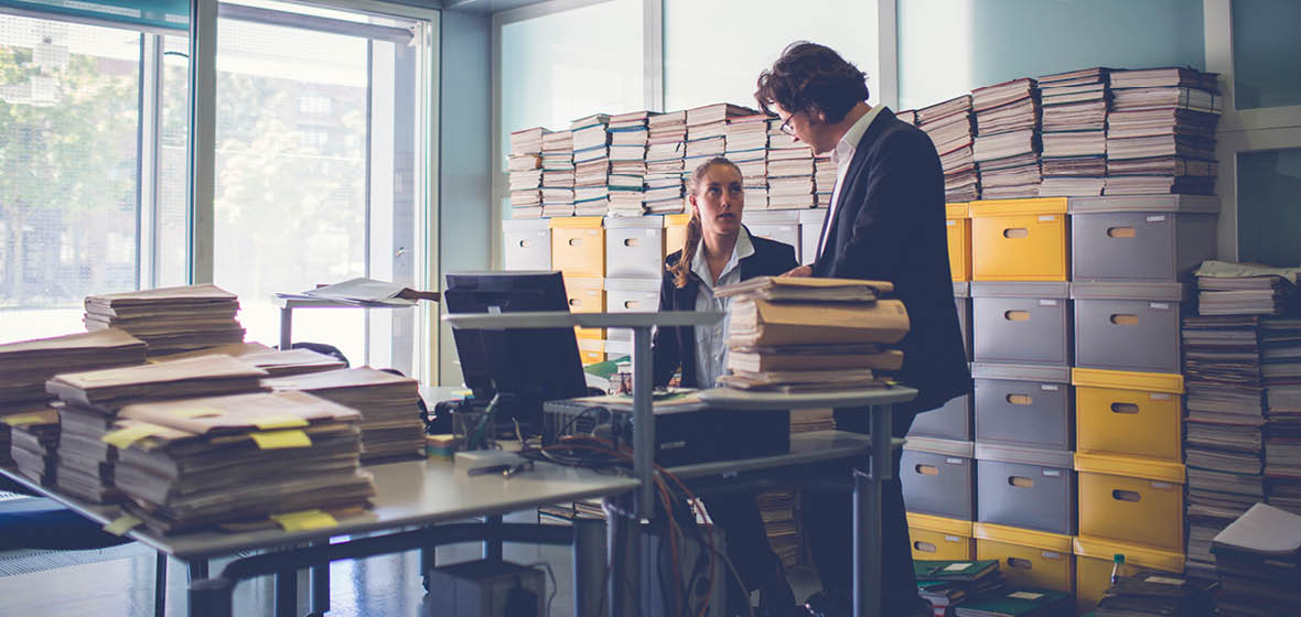Man and woman in an office surrounded by boxes of files