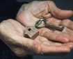 Older person's hands holding a key and a small wooden house