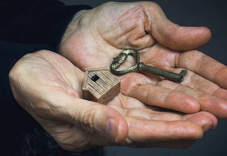 Older person's hands holding a key and a small wooden house