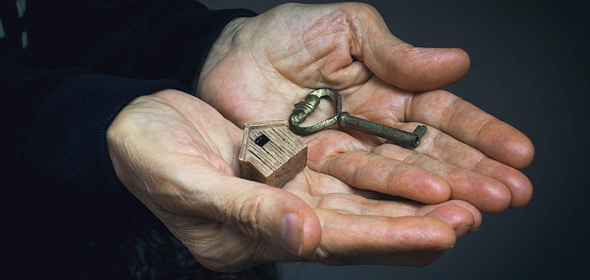 Older person's hands holding a key and a small wooden house