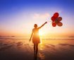 happy girl with multicolored balloons enjoying summer beach at sunset