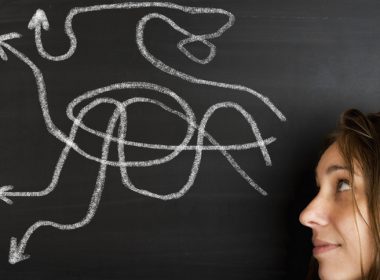 Woman's face next to a blackboard with several chalk arrows on it, pointing in different directions