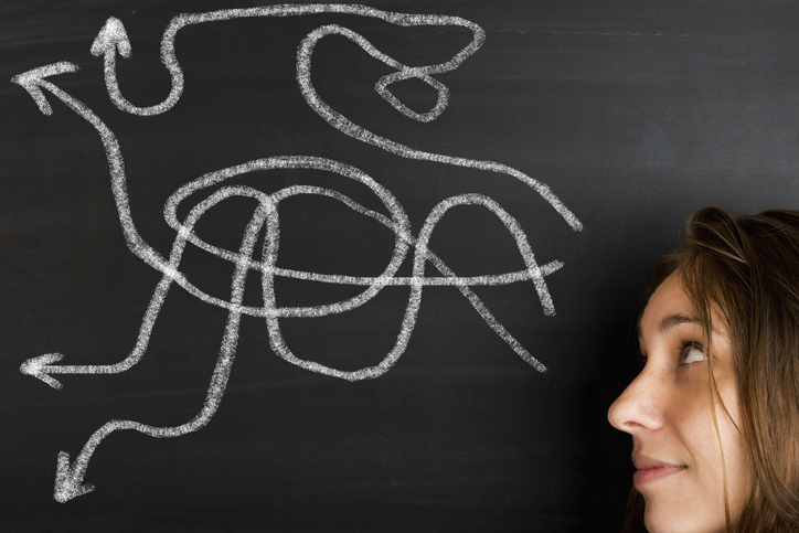 Woman's face next to a blackboard with several chalk arrows on it, pointing in different directions