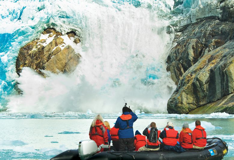 group of people in boat looking at waterfall in Alaska