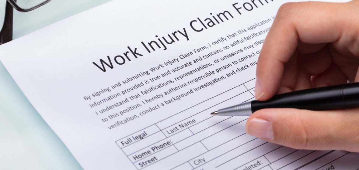 Close-up Of A Woman's Hand Filling Work Injury Claim Form
