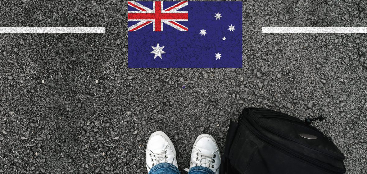 a man with a shoes and backpack is standing on asphalt next to flag of Australia and border