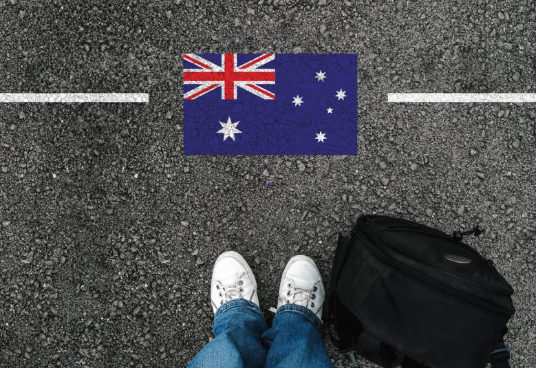 a man with a shoes and backpack is standing on asphalt next to flag of Australia and border