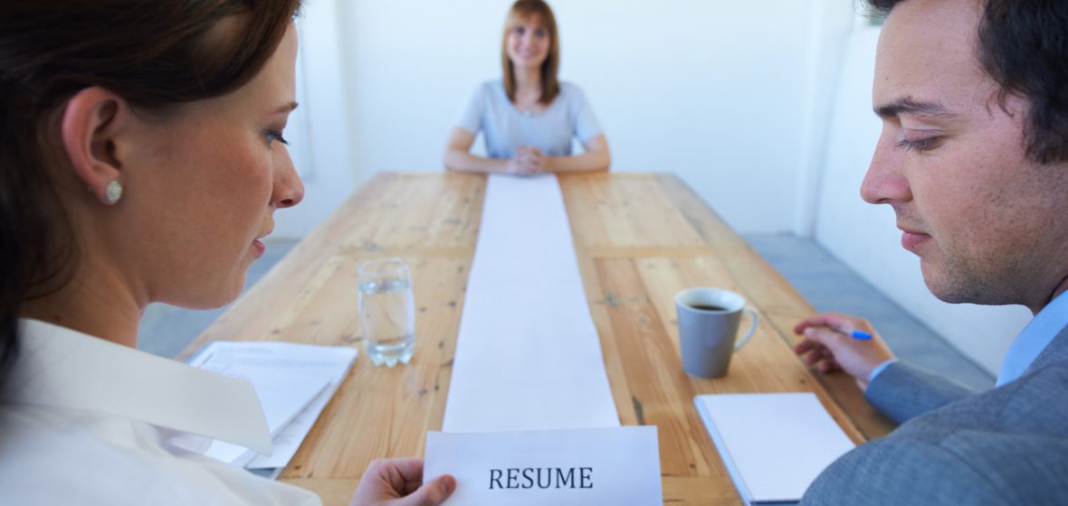 Two employers review a very long resume in front of a smiling candidate