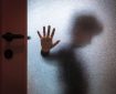Blurred sad boy leaning open hand against glass door.
