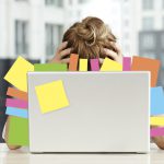 Exhausted businesswoman sits in front of a laptop covered in post-it notes