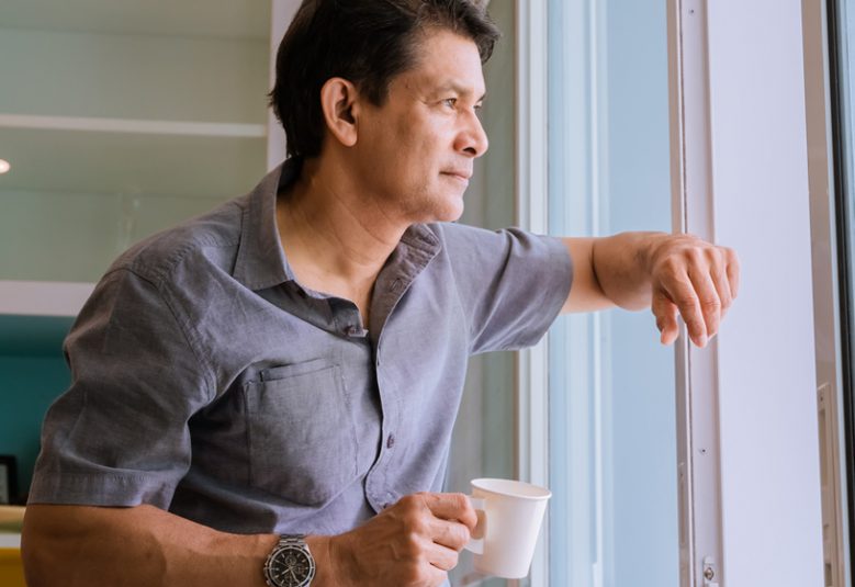 Middle-aged Asian man looking through a window, sipping coffee