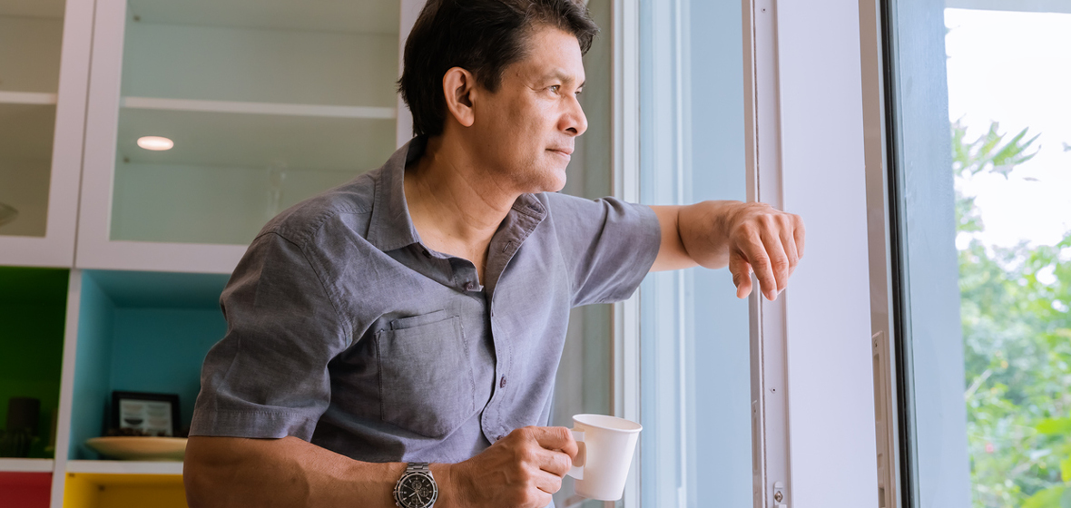 Middle-aged Asian man looking through a window, sipping coffee