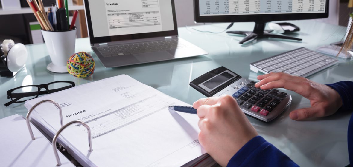 Person using a calculator reads an invoice at a desk