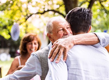 Older man hugs adult son at a party