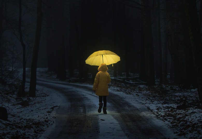 Child in a yellow raincoat, carrying a yellow umbrella walking on a road