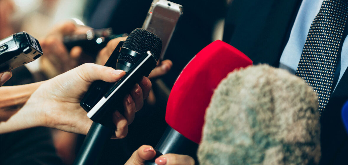 photo of hands reaching out with a microphone to portray how to work with media