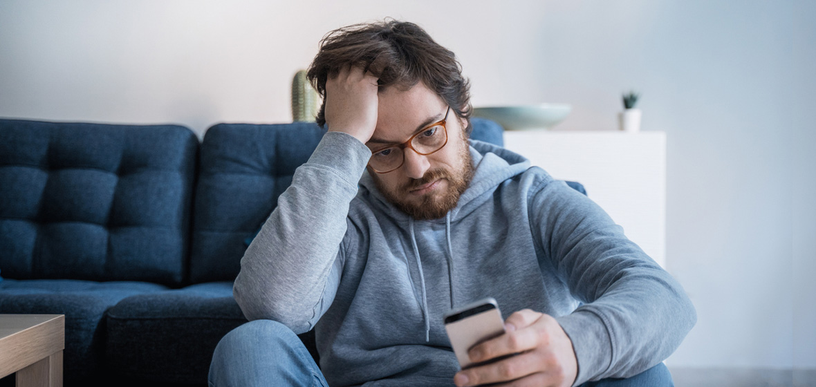 photo of man on couch looking sad and looking at mobile phone to show loneliness
