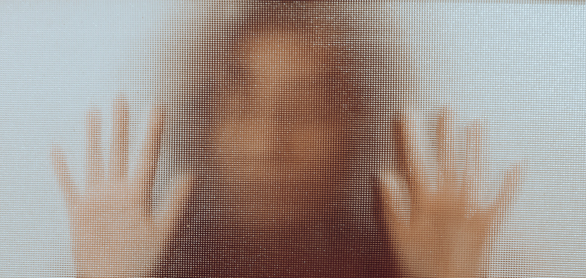 photo showing woman behind mottled glass with hands up